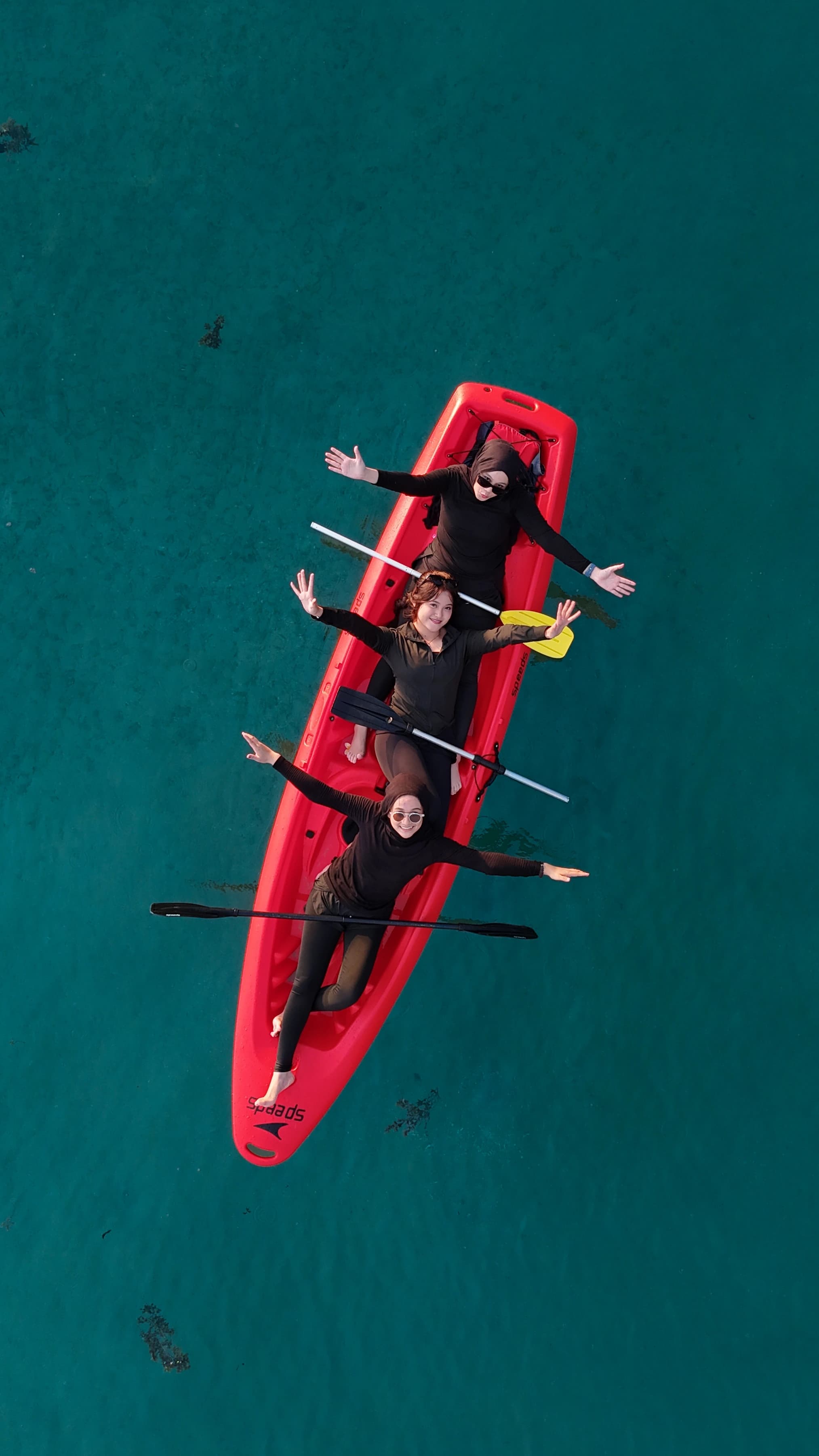 Tiga orang di atas kayak merah, dipotret dari drone
